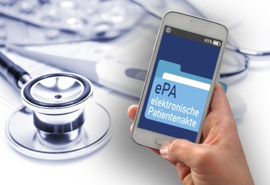 Das Bild zeigt eine Hand, die ein Smartphone hält. Auf dem Bildschirm des Smartphones ist eine Anwendung mit der Aufschrift „ePA – elektronische Patientenakte“ zu sehen. Im Hintergrund liegen medizinische Utensilien, wie ein Stethoskop und Tablettenblister.