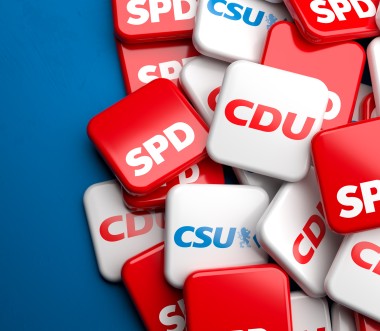 Ein Stapel quadratischer Kacheln mit den Logos deutscher Parteien: SPD (rot), CDU (rot-weiß) und CSU (blau-weiß). Die Kacheln liegen übereinander auf einem blauem Hintergrund, der links ins Bild hineinragt. Ein Stapel quadratischer Kacheln mit den Logos deutscher Parteien: SPD (rot), CDU (rot-weiß) und CSU (blau-weiß). Die Kacheln liegen übereinander auf einem blauem Hintergrund, der links ins Bild hineinragt.
