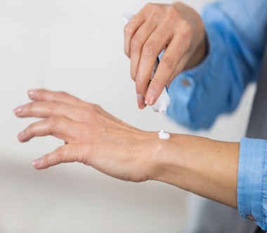 Die Nahaufnahme zeigt eine Person, die aus einer Tube eine kleine Menge weißer Creme auf den Handrücken aufträgt. Die Nahaufnahme zeigt eine Person, die aus einer Tube eine kleine Menge weißer Creme auf den Handrücken aufträgt.